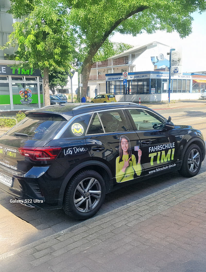 Ein schwarzes Fahrschulauto mit Beschriftungen steht auf einer Straße.