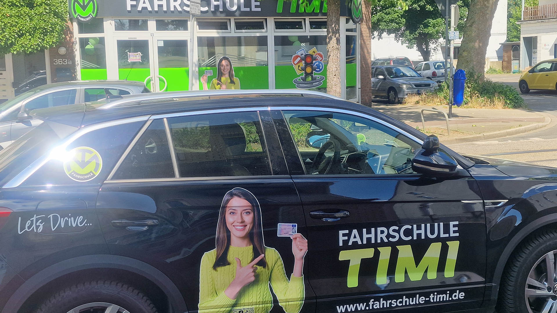 Eine dunkelblaue Fahrschulauto mit Werbung einer lächelnden Frau in grünem Pullover.