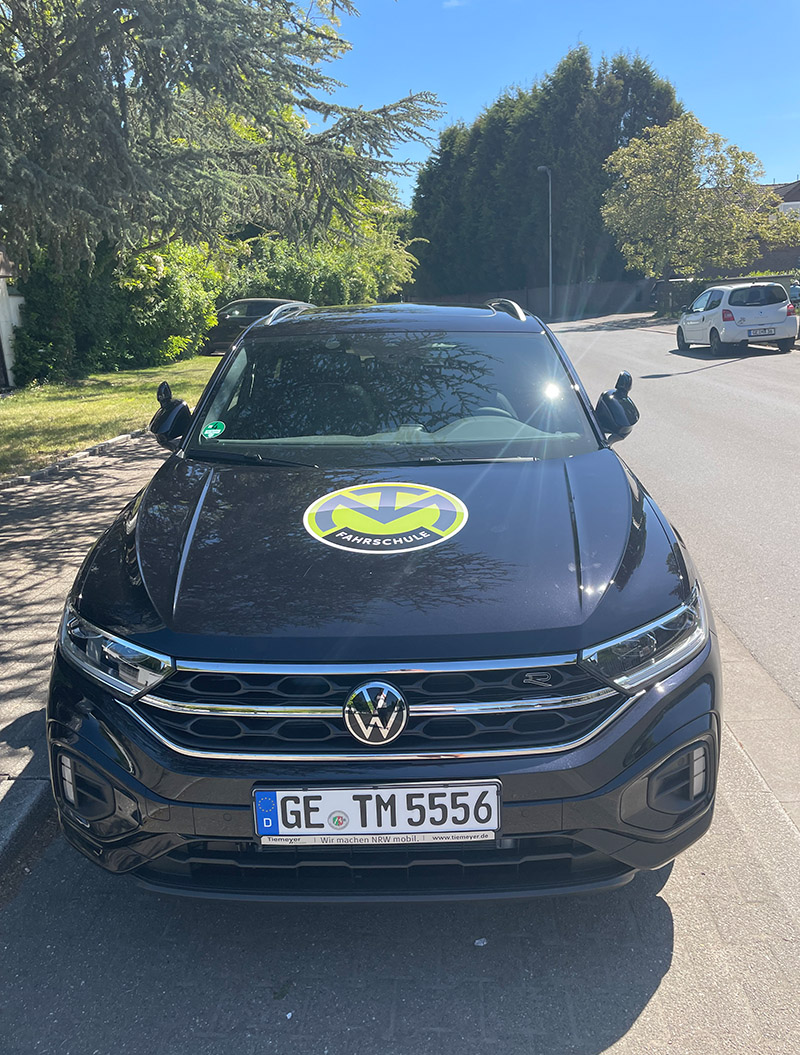 Ein schwarzer VW-SUV mit gelbem Logo auf der Motorhaube parkt auf einer Straße.