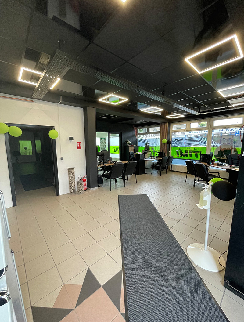 Ein modernes Büro mit dunkler Decke und großen Fenstern, Stühle und Schreibtische sind verteilt, einige grüne Dekorationen erhellen den Raum.