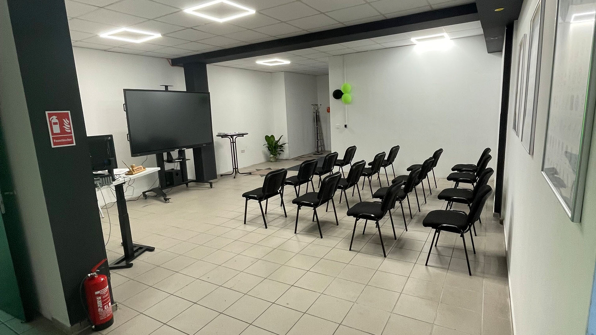 Ein leerer Konferenzraum mit schwarzen Stühlen und einem großen Bildschirm.
